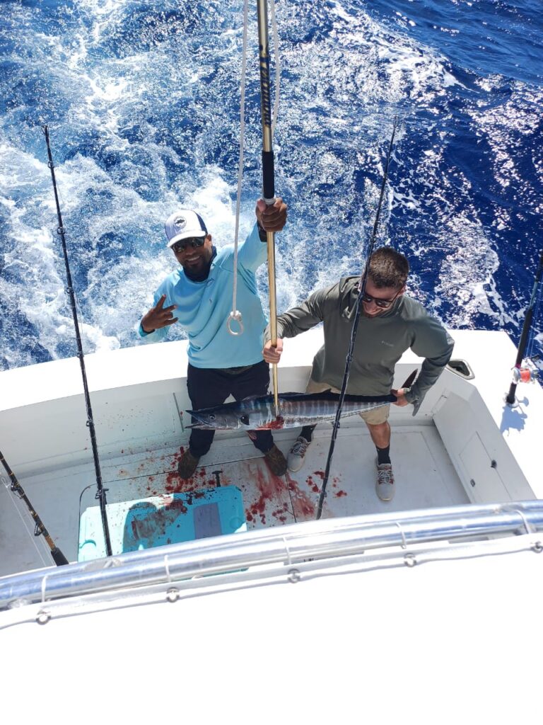 Two anglers on a sportfishing boat holding a wahoo catch over open blue ocean