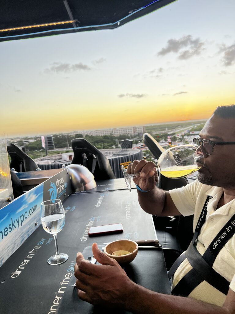 Man sipping white wine at the Dinner in the Sky table during a golden sunset