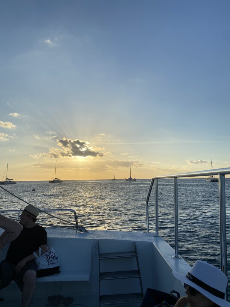 Pasajeros en un bote contemplan el atardecer con veleros anclados en el mar