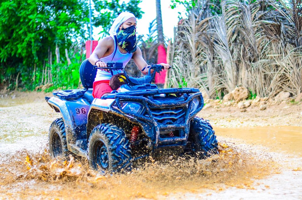 Person riding an ATV through a muddy trail with water splashing around