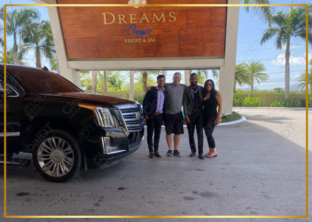 Four guests posing with a black Cadillac Escalade at the Dreams Onyx Resort and Spa entrance sign
