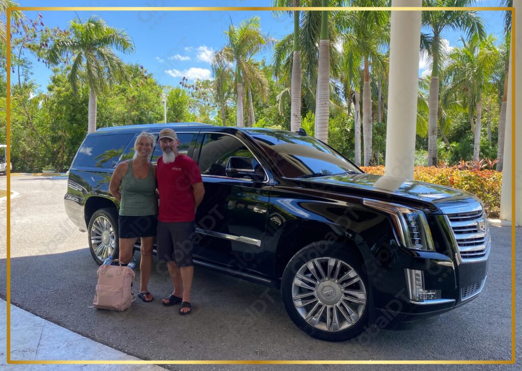 Couple posing beside a black Cadillac Escalade with luggage under palm trees on a sunny transfer