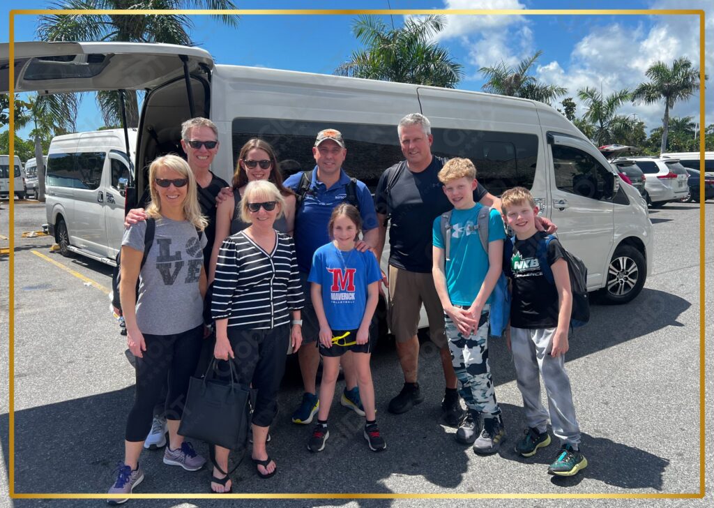 Family of nine posing in front of a white Toyota Hiace van after a GlobalDT airport transfer