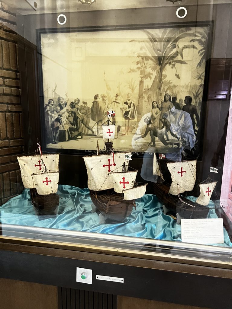 Exhibición de museo con maquetas de carabelas españolas y un mural histórico al fondo