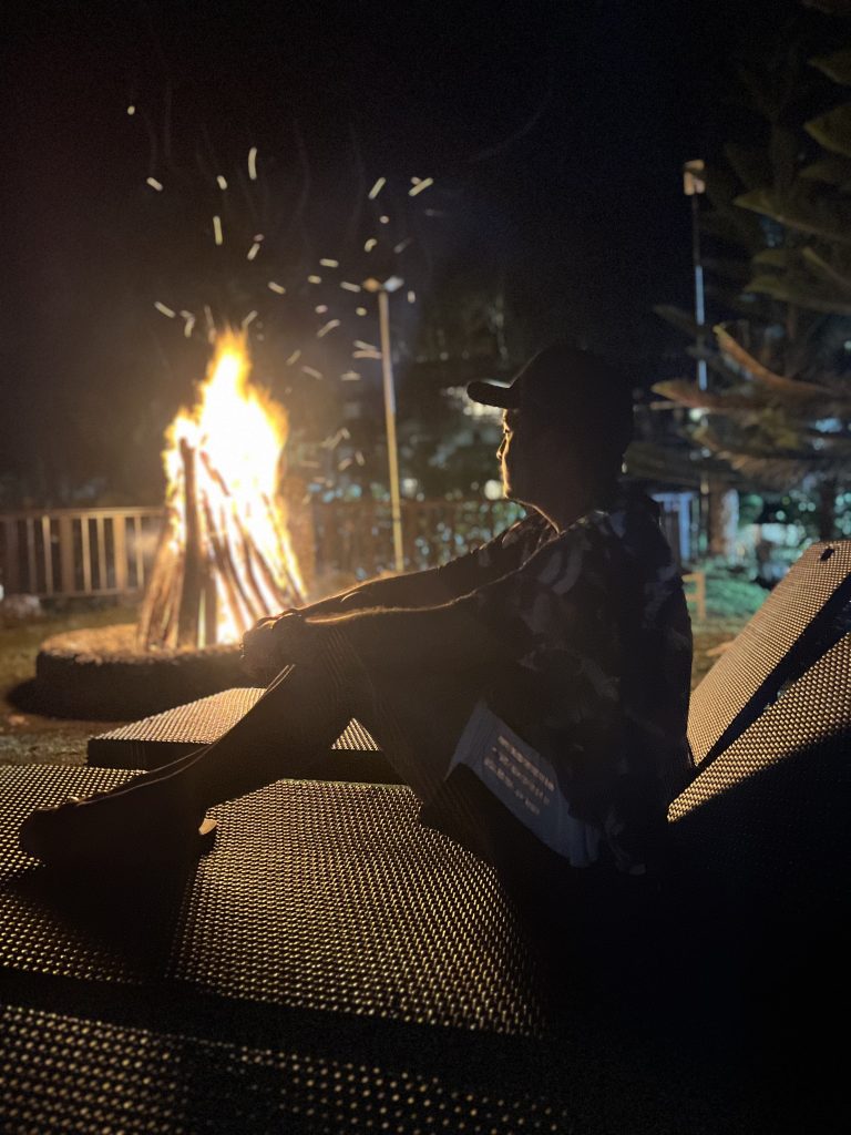 Person sitting on a lounge chair beside a bonfire at night