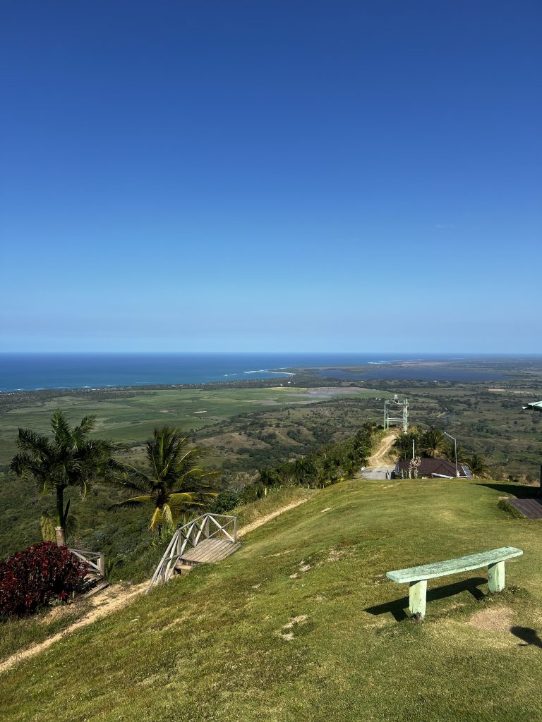 Hilltop bench overlooking green coastal plains and the sea under deep blue sky