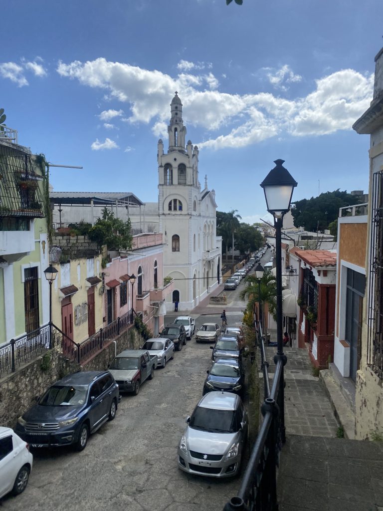 Colonial street in Santo Domingo with white church, lamppost and parked cars